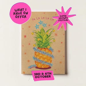 May include: A rectangular greeting card on tan paper featuring a pineapple decorated with blue tinsel, small yellow bells, and blue star illustrations. The text reads "Fa La La La La", "WHAT I HAVE ON OFFER", "SUPER SECONDS FESTIVAL", and "3RD & 4TH OCTOBER".