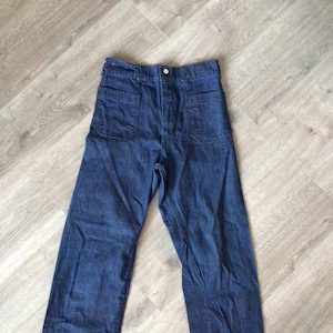 May include: Dark blue denim pants with two large back pockets and a button closure. The pants have a high waist and a straight leg design. The denim appears to be a medium weight, suitable for various seasons.