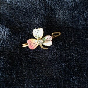 May include: A gold-tone clover pin with a white, pink and green enamel design. The clover has a single rhinestone in the centre.