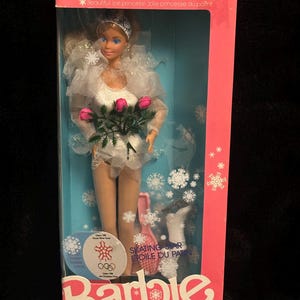 May include: A Barbie doll wearing a white skating outfit with a white fur trim and a bouquet of pink roses. The doll is holding a pair of white ice skates. The box is pink and white with the words "Skating Star" and "Etoile du patin" on it. The box also features the Olympic rings and the words "Calgary 1988" and "Olympic Winter Games".
