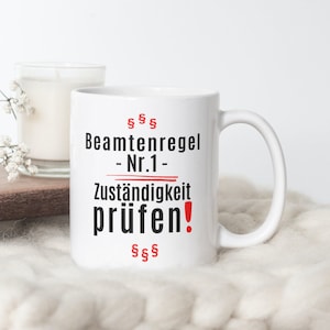 Pode incluir: Caneca de cerâmica branca com texto preto que diz "Beamtenregel - Nr. 1 - Zuständigkeit prüfen!" com um ponto de exclamação vermelho e sinais de dólar.