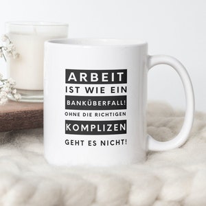 May include: White ceramic mug with a black graphic that reads "Arbeit ist wie ein Banküberfall! Ohne die richtigen Komplizen geht es nicht!"