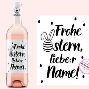 Peut inclure: Une bouteille de vin rosé avec une étiquette blanche ornée d'un motif de Pâques noir et blanc. L'étiquette comprend le texte "Frohe Ostern, liebe:r Name!" et un dessin d'un œuf de Pâques avec des oreilles de lapin.