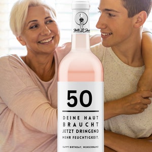 May include: A pink wine bottle with a white label that says "50" and "DEINE HAUT BRAUCHT JETZT DRINGEND MEHR FEUCHTIGKEIT. HAPPY BIRTHDAY, WUNSCHNAME!"