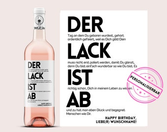 May include: A pink wine bottle with a black and white label that reads "Der Lack ist ab" and "Happy Birthday, Liebe(r) Wunschname!" The label also includes a small illustration of a bird.