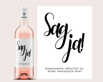 May include: A pink bottle of wine with a white label that says "Sag ja!" and "Wunschname, mochtest du meine Trauzeugin sein?"  The bottle is sitting on a white background.
