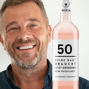 May include: A pink wine bottle with a white label that says "50" and "DEINE HAUT BRAUCHT JETZT DRINGEND MEHR FEUCHTIGKEIT. HAPPY BIRTHDAY, WUNSCHNAME!"