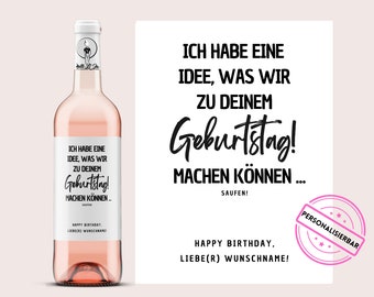 May include: A bottle of rosé wine with a white label featuring black text that reads "ICH HABE EINE IDEE, WAS WIR ZU DEINEM Geburtstag! MACHEN KÖNNEN... SAUFEN!" A matching card is next to the bottle with the same text.