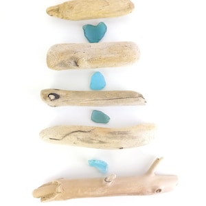 May include: Five pieces of driftwood arranged vertically, with four pieces of turquoise blue sea glass placed between them.