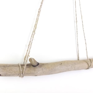 Może przedstawiać: Kawałek drewna unoszonego przez prąd z naturalną, szorstką fakturą jest zawieszony na suficie za pomocą dwóch sznurków. Drewno unoszone przez prąd jest jasnobrązowe i ma węzeł na jednym końcu.