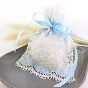 May include: A small white and blue lace bag with a light blue satin ribbon tied around it. The bag is sitting on a gray plate.