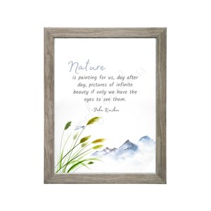 May include: A framed print featuring a watercolor illustration of mountains, grass, and a dragonfly. The print includes the quote "Nature is painting for us..." by John Ruskin in a soft blue font. The frame is a light gray color.