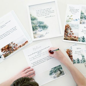 May include: A collection of nature-themed stationery and artwork. Includes a framed print, loose prints, and a binder with lined paper. The artwork features watercolor illustrations of trees, mountains, and landscapes, with quotes about nature. A person is writing on a sheet of paper.