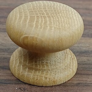 May include: A light brown wooden knob with a rounded top and a slightly smaller base. The knob has a smooth, polished finish and a subtle grain pattern.