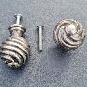May include: Two silver metal cabinet knobs with a swirl design and a silver metal screw.