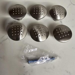 Puede incluir: Seis pomos de armario plateados con una superficie texturizada y punteada. Los pomos est&aacute;n dispuestos en dos filas de tres. Una peque&ntilde;a bolsa de pl&aacute;stico que contiene un tornillo se encuentra en la esquina inferior derecha de la imagen.