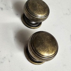 May include: Two antique brass cabinet knobs with a raised, rounded design and a smooth, slightly textured finish.