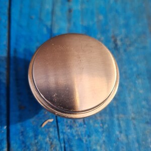 May include: A round, brushed nickel cabinet knob with a smooth, slightly raised surface.