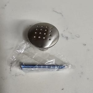 Puede incluir: Un pomo de armario plateado con un dise&ntilde;o redondo y plano y un patr&oacute;n de peque&ntilde;os agujeros. Viene con un tornillo plateado.