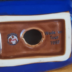 Puede incluir: Una figurita de cer&aacute;mica marr&oacute;n y azul con la inscripci&oacute;n "Wade on Tour 1997". La figurita tiene un agujero en la parte inferior y un logotipo que dice "The Official International Wade Collectors Club".