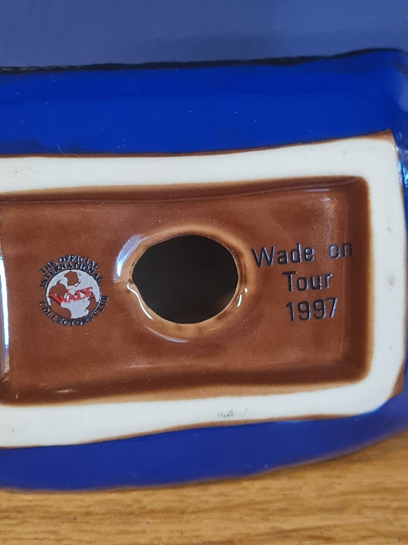 Puede incluir: Una figurita de cer&aacute;mica marr&oacute;n y azul con la inscripci&oacute;n "Wade on Tour 1997". La figurita tiene un agujero en la parte inferior y un logotipo que dice "The Official International Wade Collectors Club".