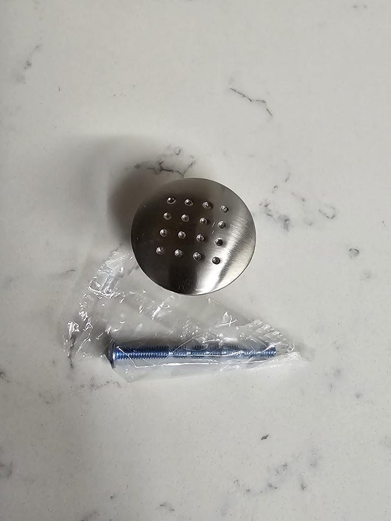 Puede incluir: Un pomo redondo de armario de plata con un patr&oacute;n de peque&ntilde;os agujeros. El pomo viene con un tornillo de plata.