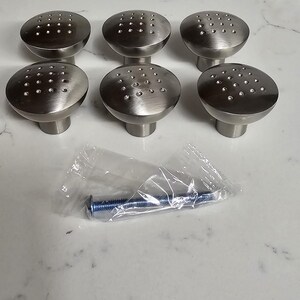 May include: Six silver cabinet knobs with a dotted pattern. The knobs are arranged in two rows of three. A single screw is included in a plastic bag.