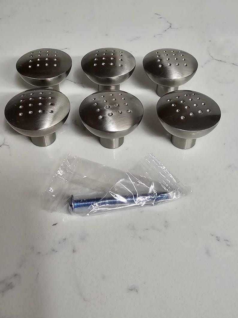 Puede incluir: Seis pomos de armario plateados con un patr&oacute;n de puntos. Los pomos est&aacute;n dispuestos en dos filas de tres. Se incluye un solo tornillo en una bolsa de pl&aacute;stico.