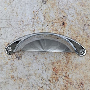 May include: A chrome cup pull cabinet handle with rounded edges and a smooth, shiny finish.
