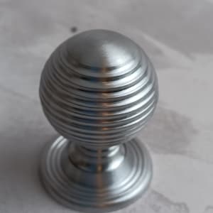 May include: A silver door knob with a ribbed design. The knob is round and has a base.