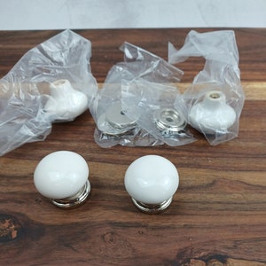May include: Set of six white ceramic cabinet knobs with silver accents. The knobs are packaged in clear plastic bags.