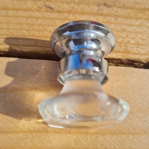 May include: A clear glass cabinet knob with a chrome base. The knob has a faceted design and a slightly frosted finish.