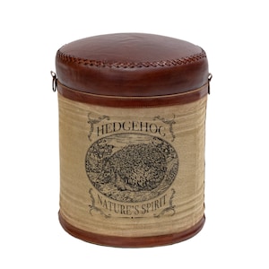 May include: A brown leather ottoman with a stitched top and a cylindrical base. The base is tan with a printed illustration of a hedgehog and the words "HEDGEHOG NATURE'S SPIRIT" in black.