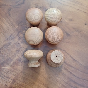 May include: Six wooden knobs in various shapes and sizes. The knobs are all a light brown colour and have a smooth, polished finish.