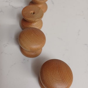 May include: Four wooden knobs with a smooth, light brown finish. The knobs are round and have a slight indentation in the centre.
