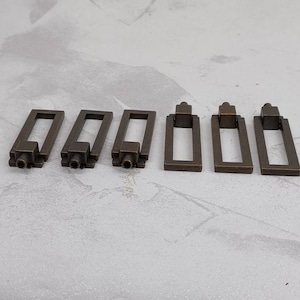 May include: Six antique brass cabinet door pulls with a rectangular shape and a small square knob on the top.