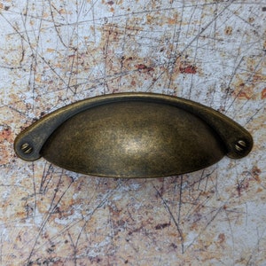 May include: A vintage-style, antique brass cabinet pull with a rounded, arched shape. The pull has a slightly distressed finish and two small screws on either side.