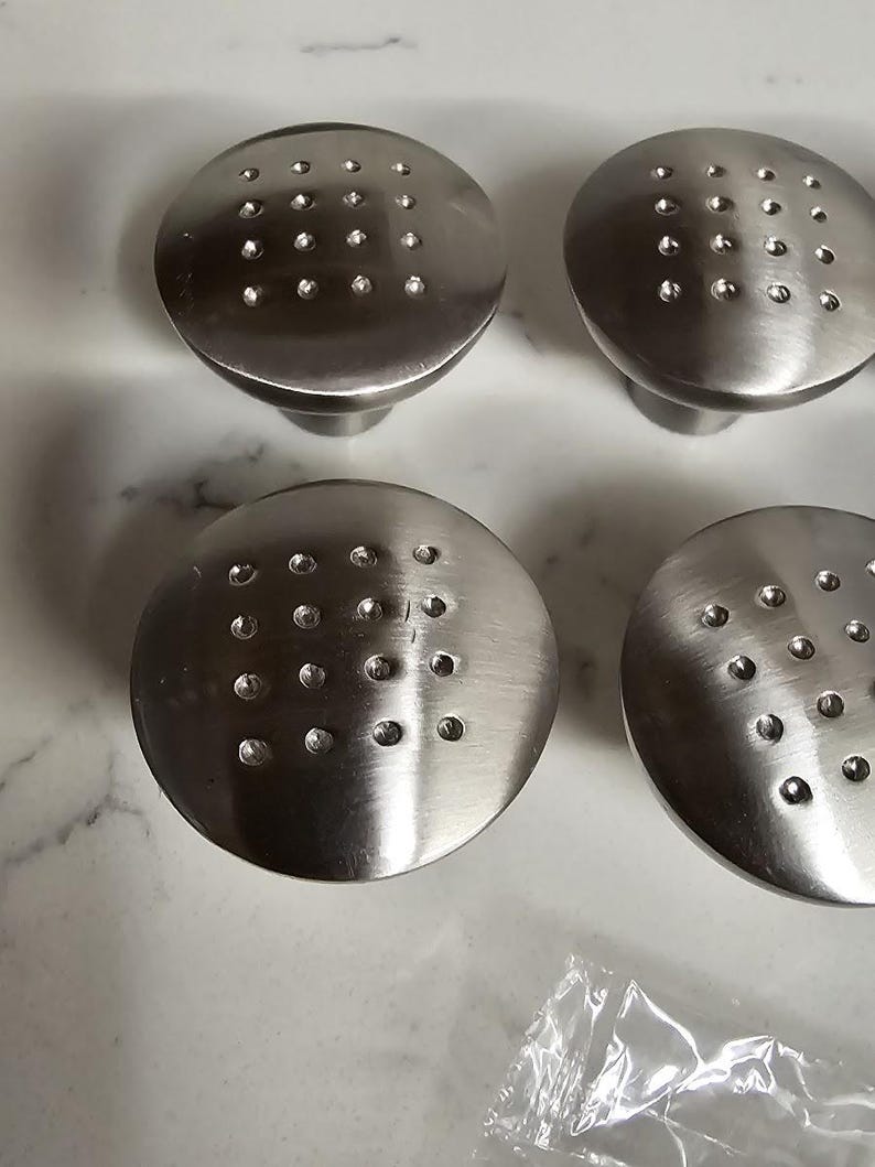 Puede incluir: Cuatro pomos de armario plateados con un dise&ntilde;o circular y una superficie texturizada. Cada pomo tiene un patr&oacute;n de peque&ntilde;os puntos espaciados uniformemente.