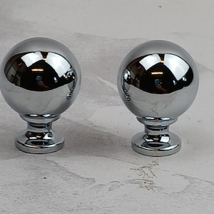 May include: Two chrome-plated round cabinet knobs with a smooth, shiny finish. The knobs have a round base and a spherical top.