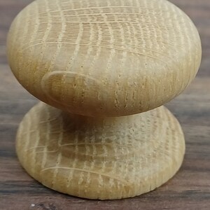 May include: A wooden knob with a round top and a cylindrical base. The knob is made of light brown wood with a grain pattern.
