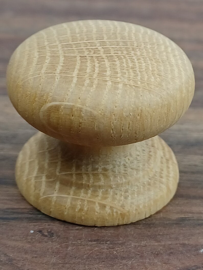 May include: A wooden knob with a round top and a cylindrical base. The knob is made of light brown wood with a grain pattern.