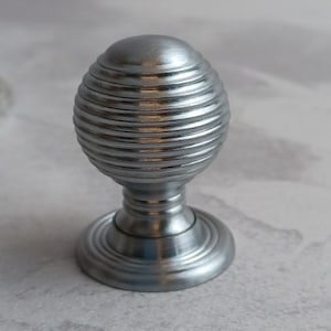 May include: A silver door knob with a round, ribbed top and a circular base.
