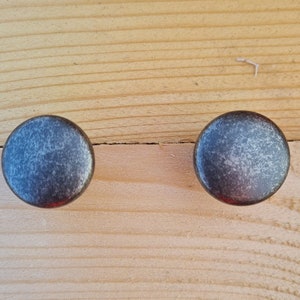 May include: Two round, silver-toned cabinet knobs with a distressed finish. The knobs are on a light wood surface.