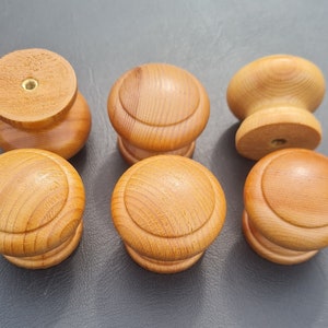 May include: Six wooden knobs with a light brown finish. The knobs have a rounded top and a slightly raised edge around the top. The knobs are all the same size and shape.