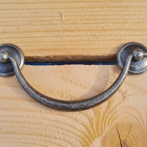 May include: A silver-toned metal drawer pull with a rounded, arched shape. The pull has a decorative knob on each end.