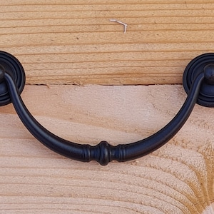 May include: Black metal cabinet pull with a rounded, curved design. The pull has a decorative knob on each end.