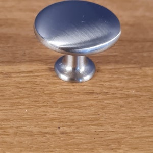 May include: A round, brushed nickel cabinet knob with a smooth, slightly domed top.