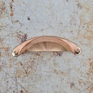 May include: A rose gold cabinet knob with a curved, rounded shape. The knob has a smooth, polished finish.