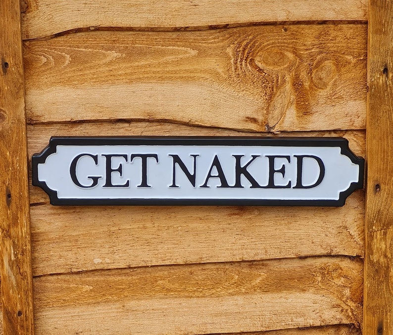 May include: A white sign with black trim and the text "GET NAKED" on a wooden background.