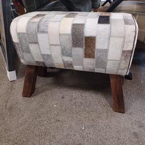 May include: A grey and brown patchwork upholstered footstool with wooden legs.